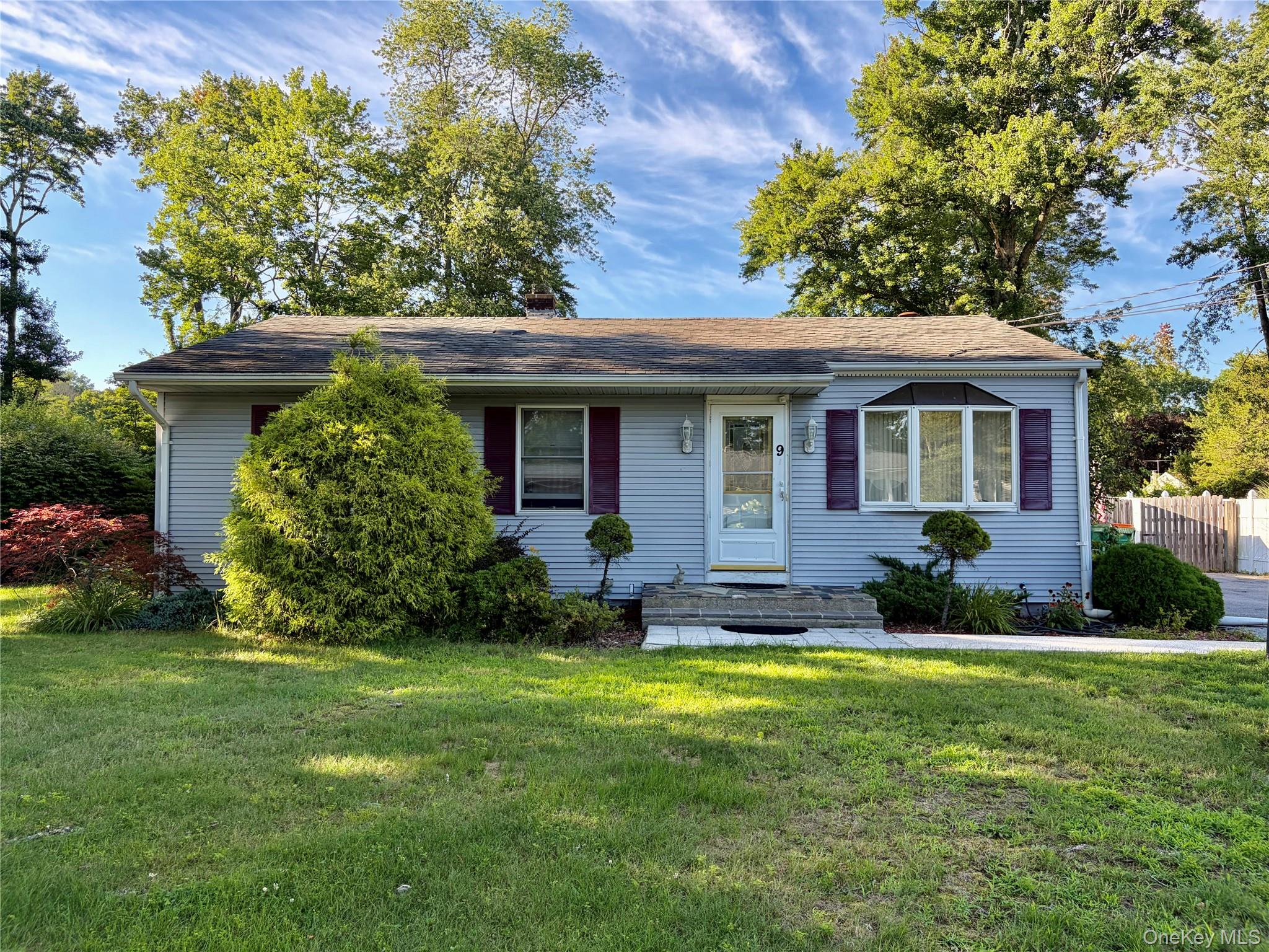 Light blue vinyl siding exterior with a shingled roof, featuring a bay window with decorative shutters, a white entry door, and manicured landscaping