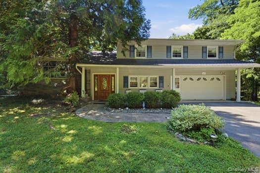 Split-level residence featuring a front entry door, portico, integrated two-car garage, and established landscaping